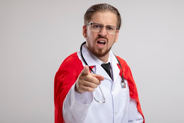 Free photo unpleased young superhero guy wearing medical robe with stethoscope and glasses showing you