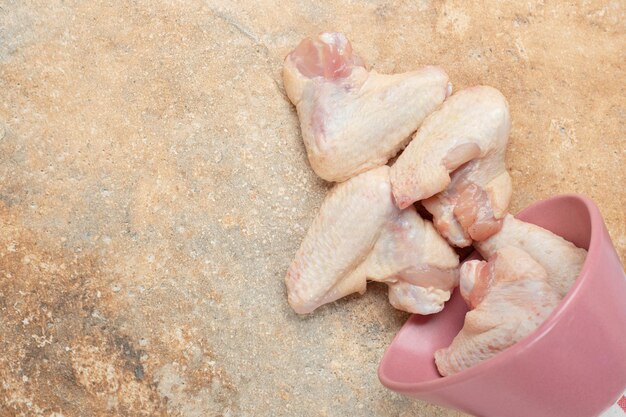 Бесплатное фото Неподготовленные куриные ножки в розовой тарелке на мраморной поверхности.