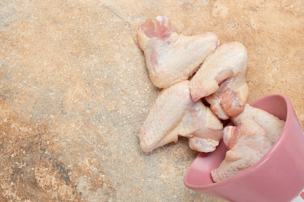 Unprepared chicken legs in pink plate on marble surface.