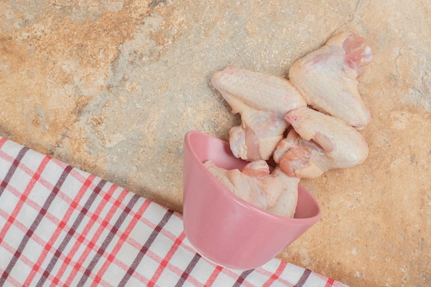 Unprepared chicken legs in pink plate on marble surface