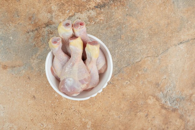 Unprepared chicken legs in white plate on marble surface.