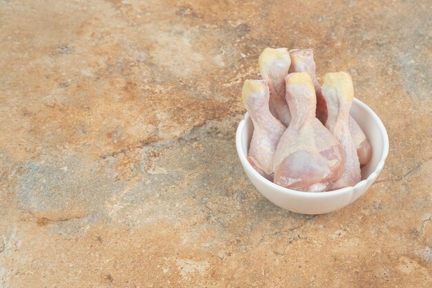 Неподготовленные куриные ножки в белой тарелке на мраморной поверхности
