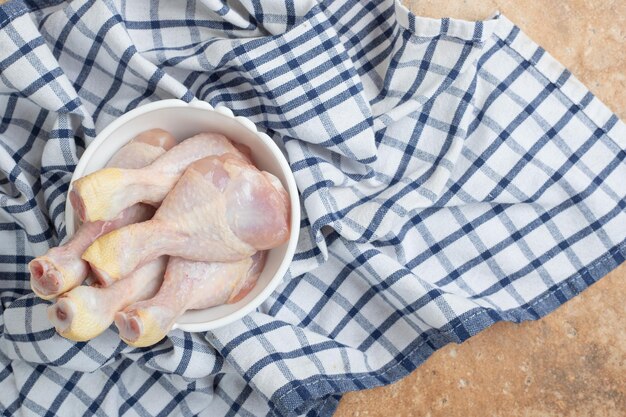 Unprepared chicken legs in white plate on tablecloth