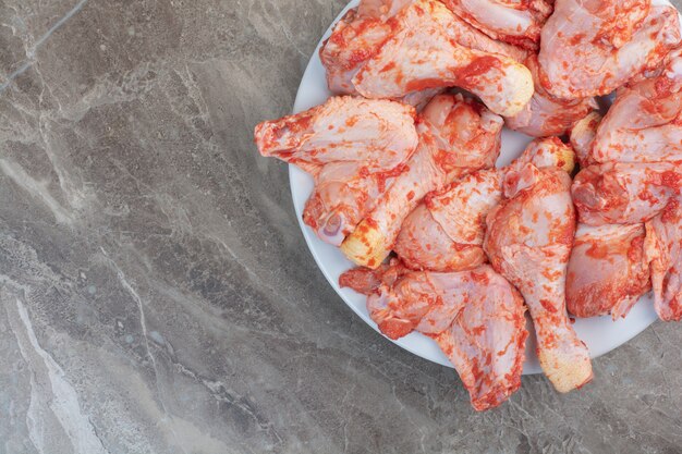 Unprepared chicken legs with spices on white plate