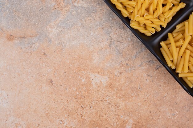 Unprepared fresh macaroni on dark plate