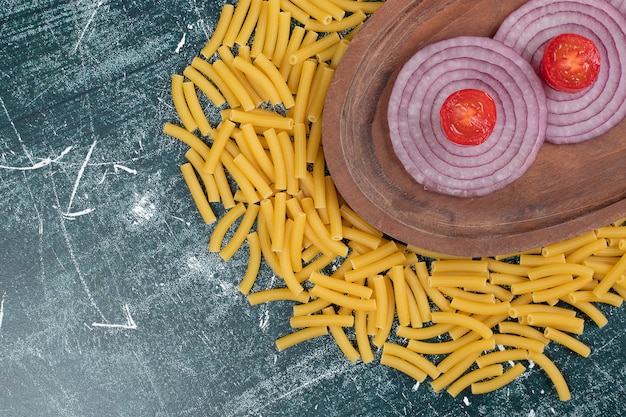 Free photo unprepared fresh macaroni with slices of onion and tomato cherry. high quality photo