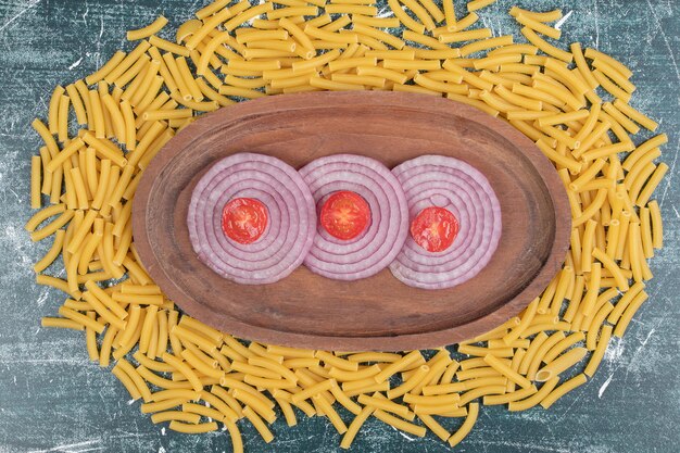 Maccheroni freschi non preparati con fettine di cipolla e pomodoro ciliegino.