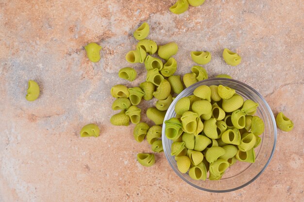 Unprepared green macaroni in glass plate on marble background. High quality photo