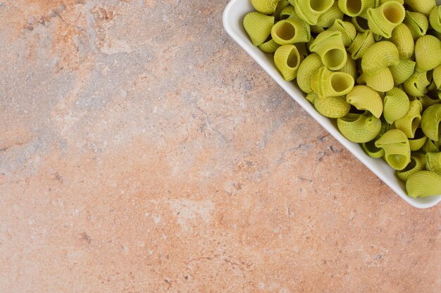 Unprepared green macaroni in white plate on marble background. High quality photo