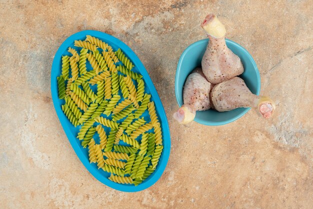 Unprepared spiral macaroni with chicken legs on blue plate.