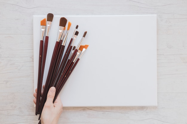 Free photo unrecognizable artist holding paintbrushes and blank paper