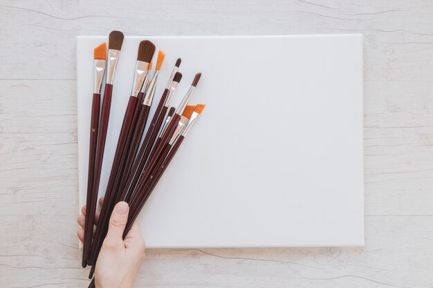 Unrecognizable artist holding paintbrushes and blank paper