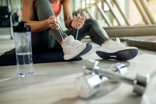 Unrecognizable athletic woman tying sports shoe at health club