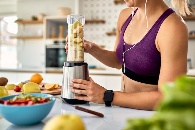 Unrecognizable athletic woman using blender while making fruit smoothie in the kitchen