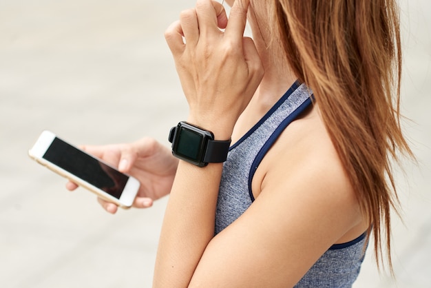 Free photo unrecognizable athletic woman with smart watch checking pulse and using smartphone