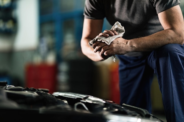 Free photo unrecognizable auto mechanic cleaning his dirty hands after repairing car engine in a workshop
