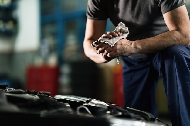 Unrecognizable auto mechanic cleaning his dirty hands after repairing car engine in a workshop