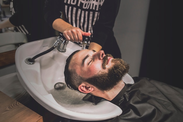 Unrecognizable barber washing head of client