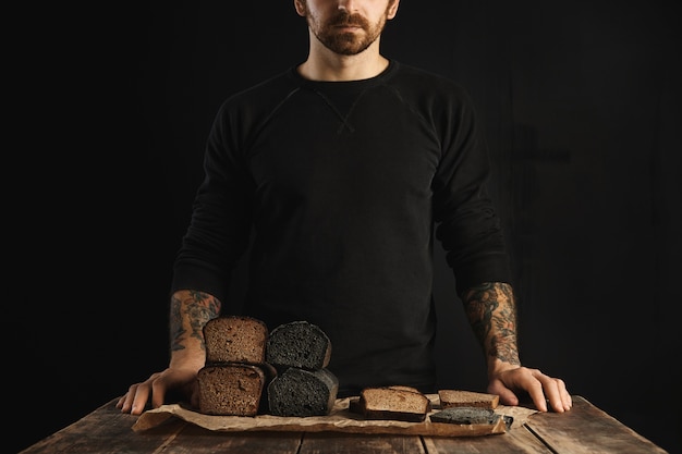 До неузнаваемости бородатый татуированный мужчина продает свежеиспеченный диетический здоровый хлеб