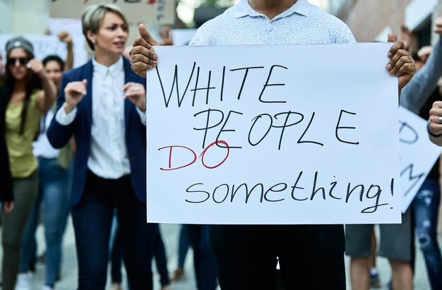 Unrecognizable black man holding placard with White people do something inscription while taking a part in Black Lives Matter protest