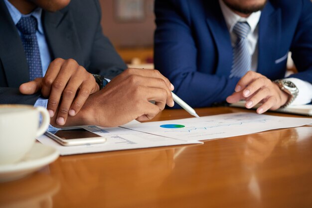 Unrecognizable businessmen sitting at table at meeting and analyzing graphs