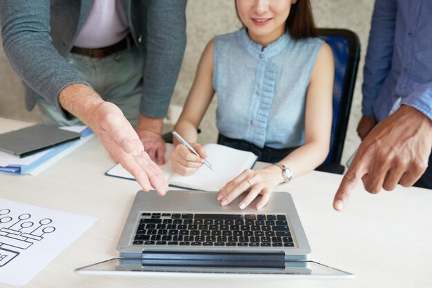 Unrecognizable colleagues looking and pointing at laptop screen at work meeting