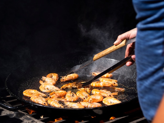 Unrecognizable cook flipping shrimps frying on big pan