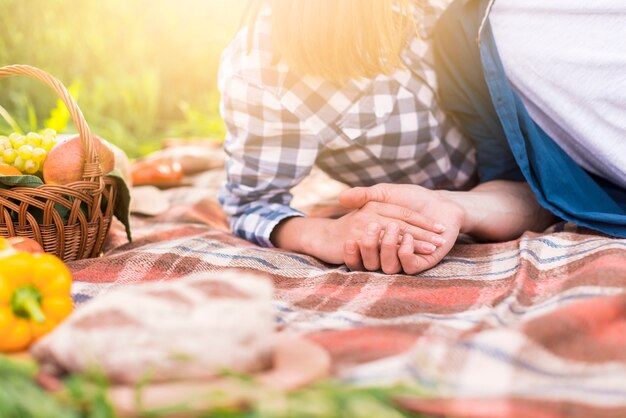 Unrecognizable couple lying on blanket and holding hands
