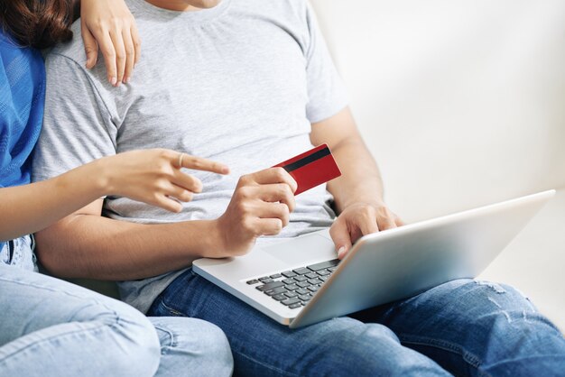 ノートパソコンとクレジットカードを保持している男とソファに座っている認識できないカップル