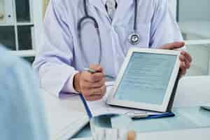 Free photo unrecognizable doctor extending the digital tab for anonymous patient to fill in the questionnaire