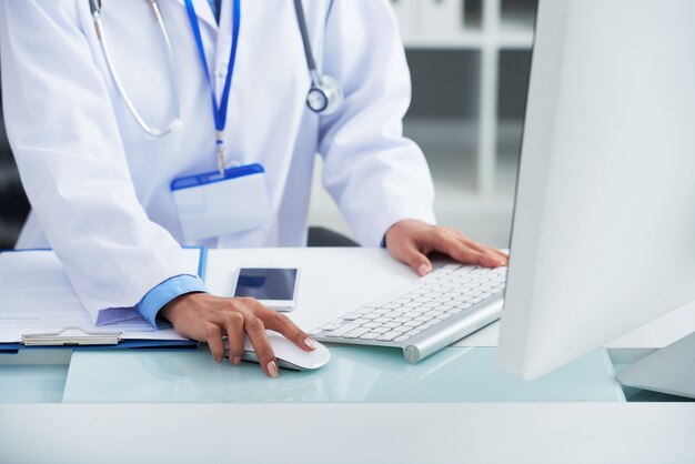 Unrecognizable doctor in white coat using computer at work