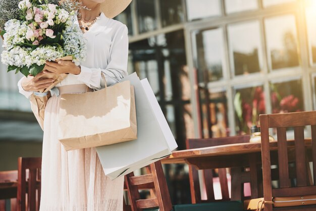 Unrecognizable elegant woman standing near street cafe with flower bouquet