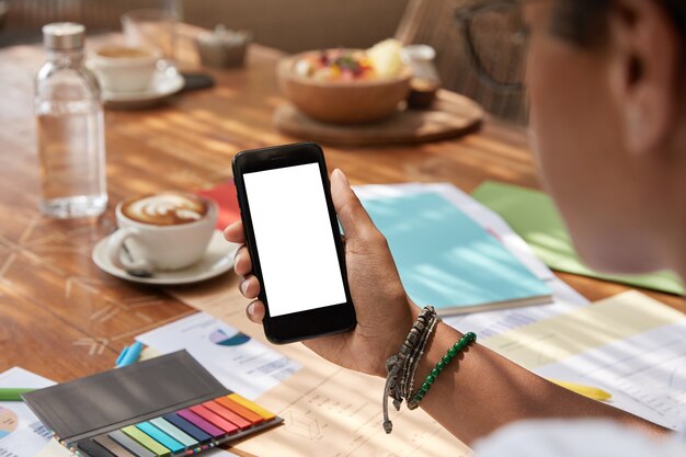 Unrecognizable ethnic young woman holds modern smart phone with blank screen