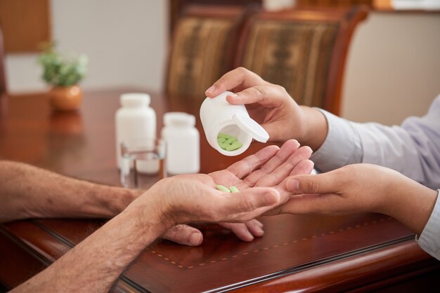 Unrecognizable female doctor giving pills to male patient during house call