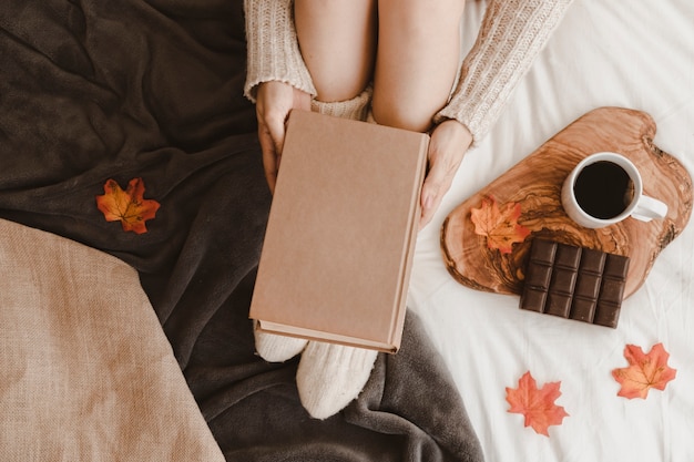 Unrecognizable female with book near tea and chocolate