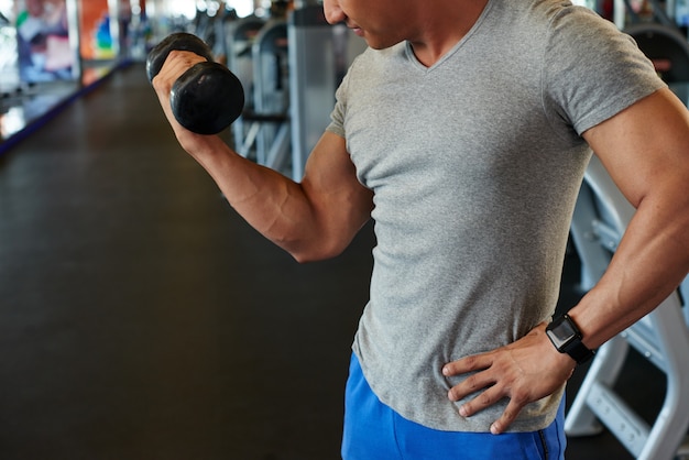 Unrecognizable fit man doing bicep curl with barbell in gym