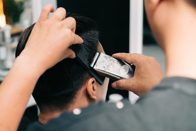 Unrecognizable hairstylist cutting customer's hair with trimmer and comb