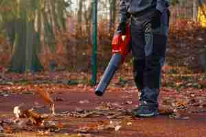 Free photo unrecognizable maintenance man wearing blue uniform and gloves working with portable leaf blower in