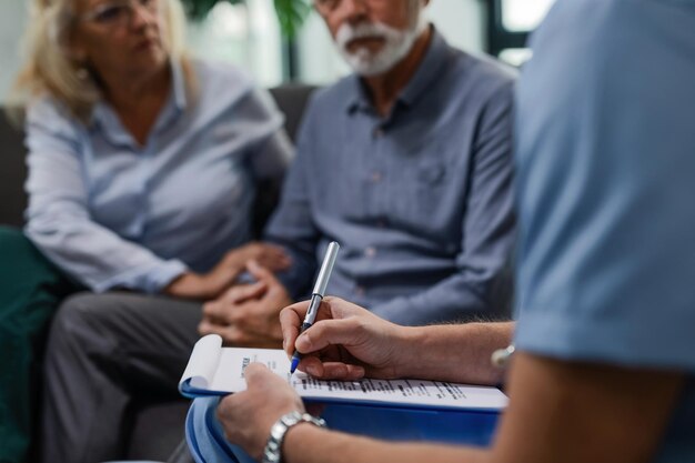 Unrecognizable male doctor writing medical report while visiting senior couple at their home