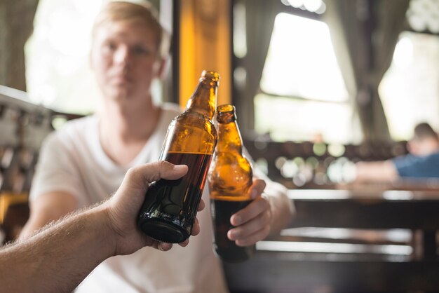 Unrecognizable male friends clinking bottles in bar