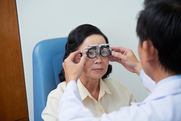 Unrecognizable male ophtalmologist fitting trial lens frame for senior female patient