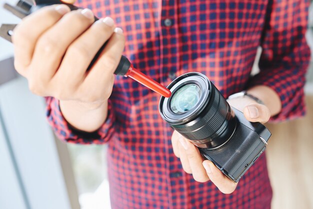 Неузнаваемый мужчина фотограф чистит объектив камеры с воздуходувкой