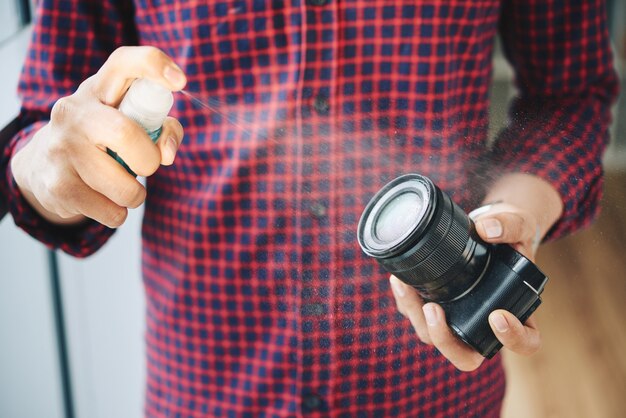 Unrecognizable male photographer spraying camera lens with cleaning fluid