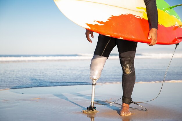 Unrecognizable male surfer standing with surfboard on sea beach