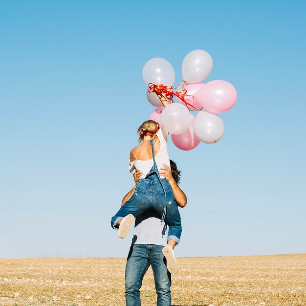 Неузнаваемый мужчина держит женщину с воздушными шарами
