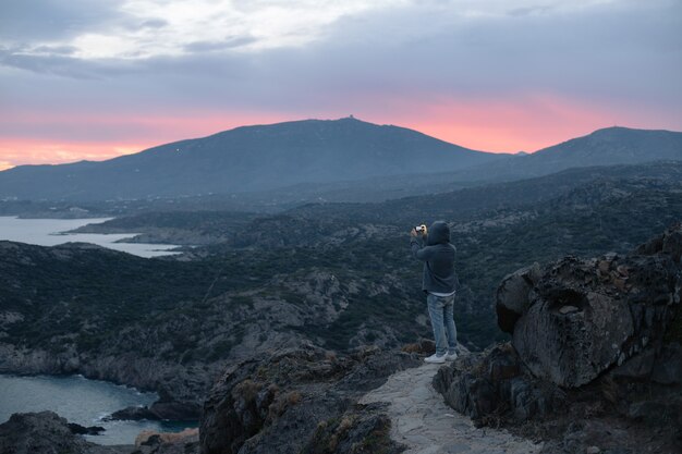 Unrecognizable man in hoodie stands on top of hiking trail on mountain