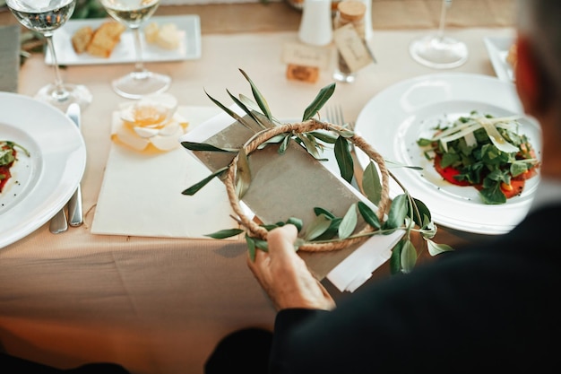 Unrecognizable man sitting at dining table and holding wedding invitation at reception hall