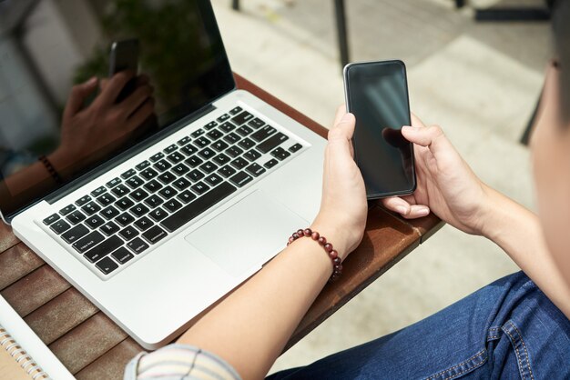 Неузнаваемый мужчина сидит с ноутбуком в кафе и с помощью смартфона