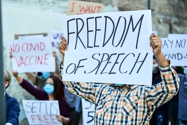 Бесплатное фото Неузнаваемый мужчина со знаменем свободы слова марширует с группой людей на акции протеста во время пандемии коронавируса