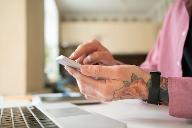 Unrecognizable man with rose tattoo using smartphone